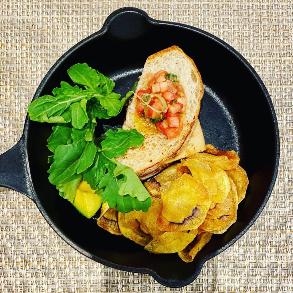 Tomato bruschetta on toasted bread served with fresh arugula, avocado, and crispy chips in a cast-iron skillet